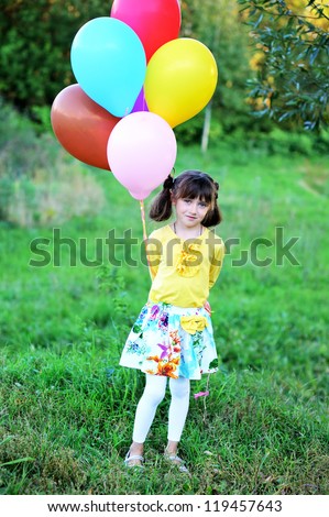 Outdoor portrait of little girl holding bunch of balloons