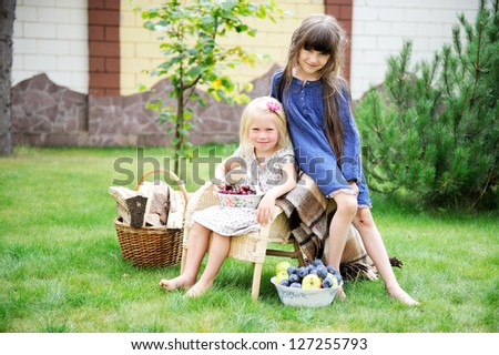 Two happy smiling girls having picnic on a green lawn in front of country house