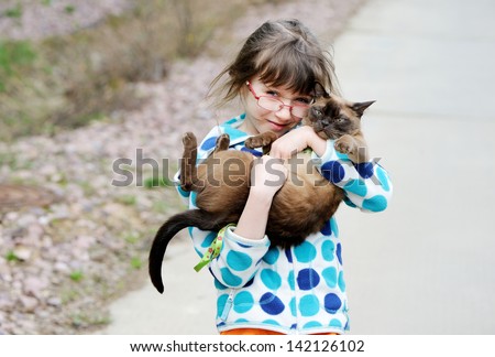 Cute young girl holding her kitty during a walk outside