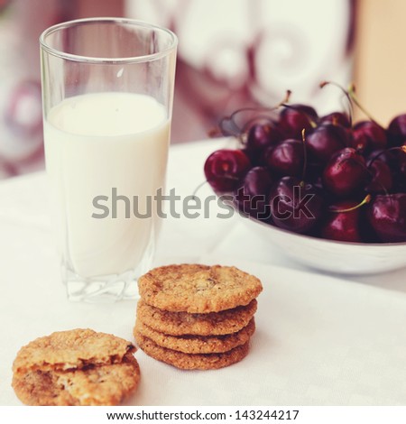 Square tone photo of glass of milk with cookies  and plate of cherries on the outdoor table