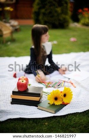 Nice young girl in navy school uniform on white blanket with books and flowers  drawing red apple with focus on books and flowers