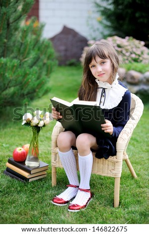 Nice young girl in navy school uniform reading the book in the garden