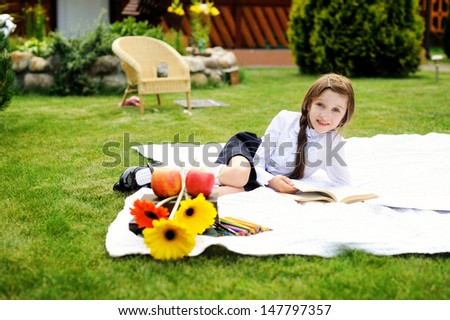 Happy young girl reading book on the white blanket in the garden