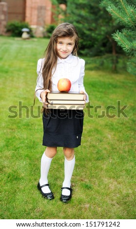 Young girl in school uniform holding stack of books with apple on top