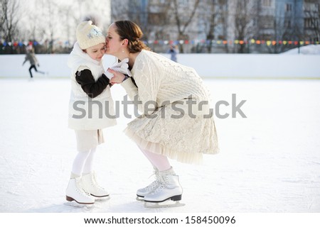 Adorable young mother with her daughter in white clothes on the ice rink