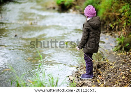 Little girl in purple hat standing by river in autumn forest