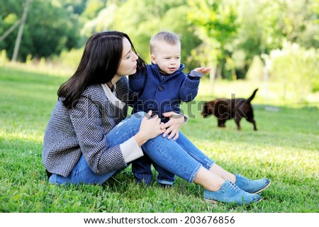 Young beauty mother hugs her cute baby son outdoors on the green lawn in the park
