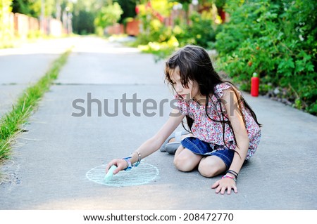 Beauty kid school age girl drawing with chalks on the road in the sunny summer evening