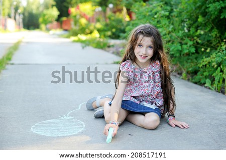 Beauty kid school age girl drawing with chalks on the road in the sunny summer evening
