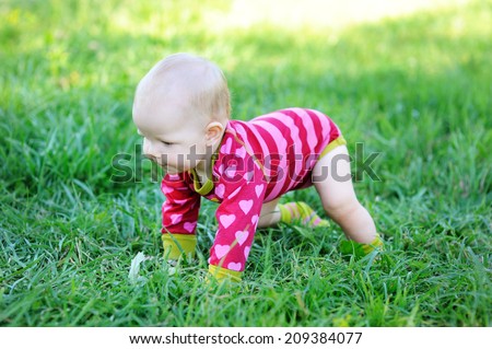Lovely baby girl  trying to get up outdoor on the green lawn at the warm day