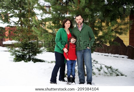 Happy family of three in the red green sweaters outdoor near the house  at the snow winter day