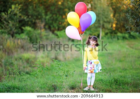 Adorable kid girl in colorful fashion outfit run  with bunch of colorful balloons in the field at the warm autumn day