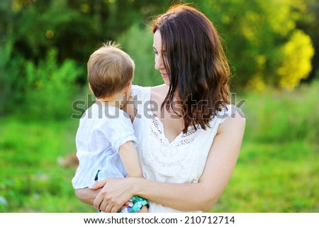 Young beauty mother hugs her cute baby son outdoors in the park