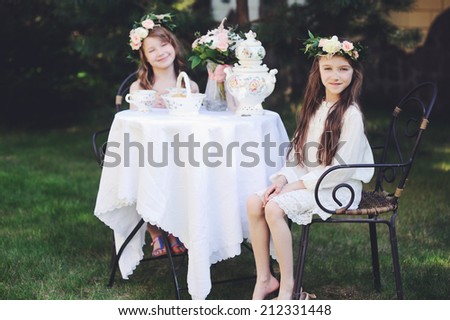 Two adorable kid girls with flower wrearth having tea in the garden. Retro style