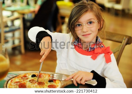 Adorable kid girl in sweater and glasses eating pizza in italian restaurant