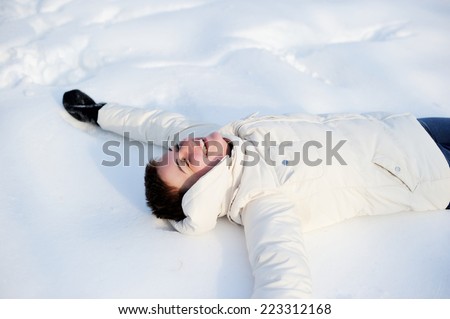 Beautiful young woman laying down on a snow and making angel figure