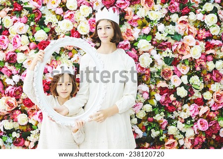 Two beauty smiling  school aged girls in white crowns and dresses over flower wall