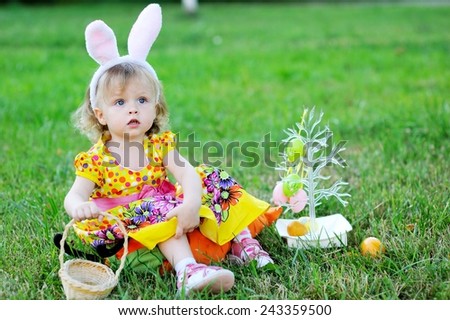 Adorable toddler girl wearing bunny ears playing with Easter eggs  sitting in a sunny garden