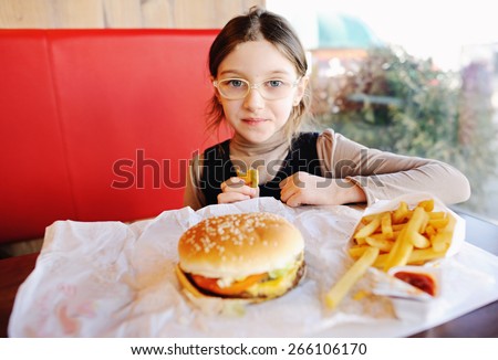 Cute little  girl in school uniform  eating a hamburger and potatoes in the restaurant