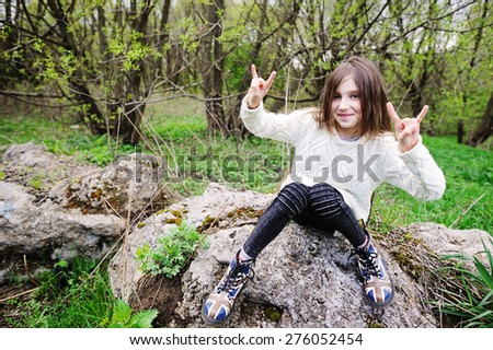 Little girl sitting on the stone in the park and making funny faces in rock style