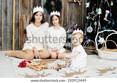 Three sisters age of 10 month, 7 and 12 years in white dresses and crowns posing in front of the christmas tree