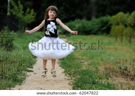 Adorable toddler girl in white tutu skirt with very long dark fluttering hair jumping on country road
