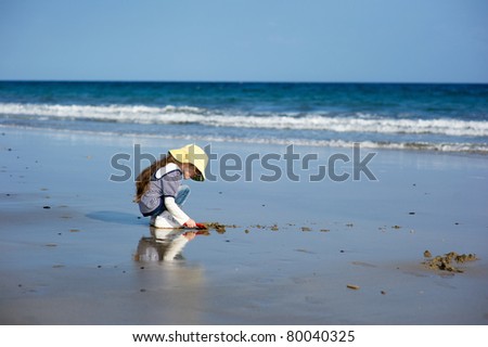 Little girl in yellow sunhat  plays on the ocean beach in cool day
