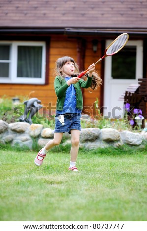 Beauty active little girl with long brunette hair in green and blue clothes plays badminton  in the backyard