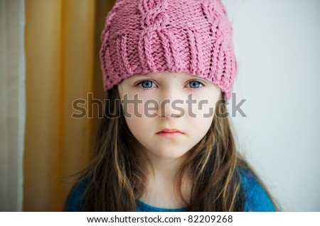 Close-up portrait of adorable sad child girl wearing pink knitted hat