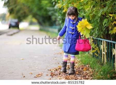 Funky little girl in blue coat walking down the street with bunch of leaves and pink bag