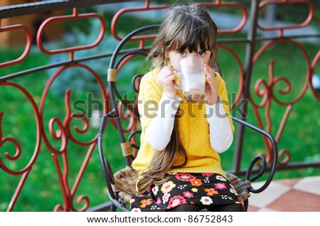 Cute child girl with a cup of milk tea having a meal outdoors