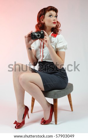 A pretty pin-up girl with a vintage camera on a soft pink background.