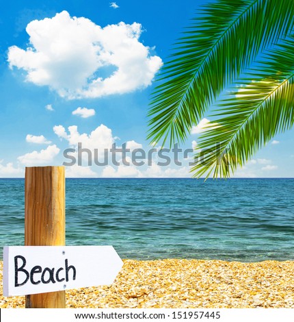 Paradise beach and sea with wooden board showing direction to the beach