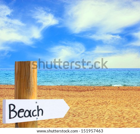 Paradise beach and sea with wooden board showing direction to the beach