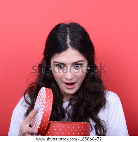 Portrait of happy woman opening gift box against red background