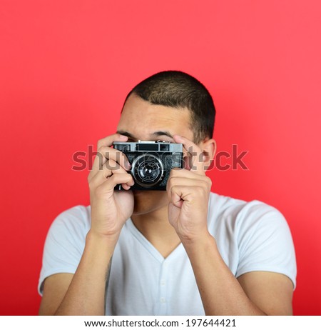 Portrait of young male holding vintage camera against red background