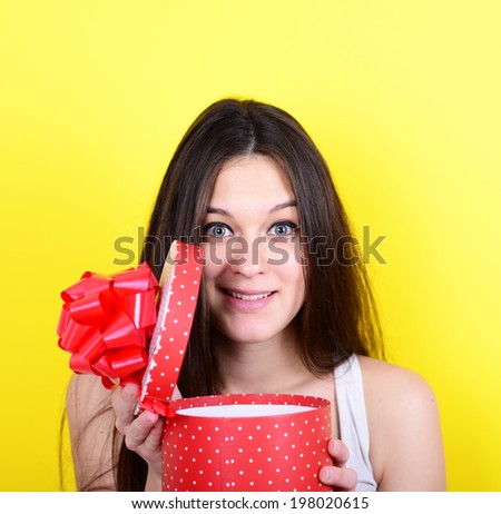 Portrait of happy woman opening gift box against yellow background
