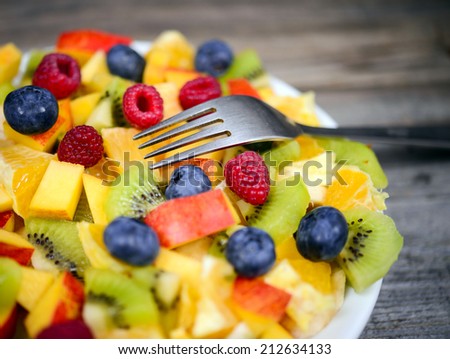 Macro shot of a fresh fruit salad with bananas kiwi orange blueberries and peach with fork