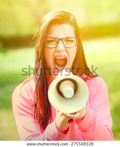 Portrait of middle aged woman shouting using megaphone against a nature background