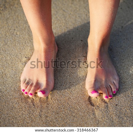 Beach travel - woman walking on sand beach leaving footprints in the sand. Closeup detail of female feet and golden sand beach