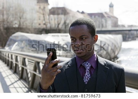 Black business man with black smart phone and modern and old architecture in background. Grey suit with violet chemise