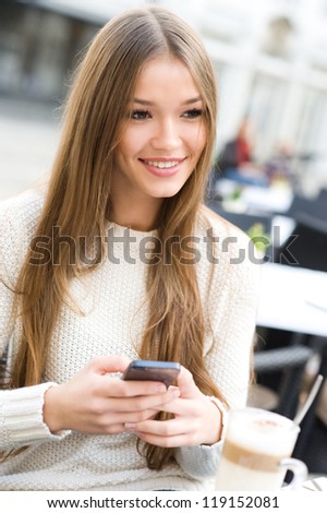 Young beauty woman writing message on cell phone in a street cafe. Looking away
