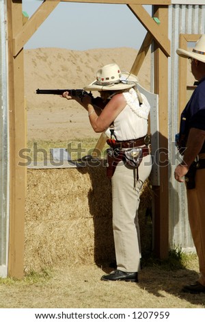 Woman competitor shooting a lever action rifle in a cowboy shoot competition.