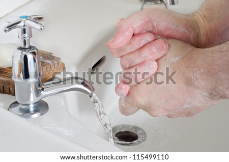 Male hands being washed in old china sink with water running from stainless steel tap, and a bar of soap resting on a wooden soap dish.