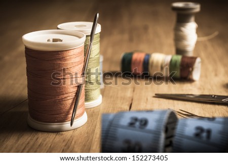 An old style image of cotton reels and other sewing items on a wooden table. Image has been aged to give a retro or vintage style.