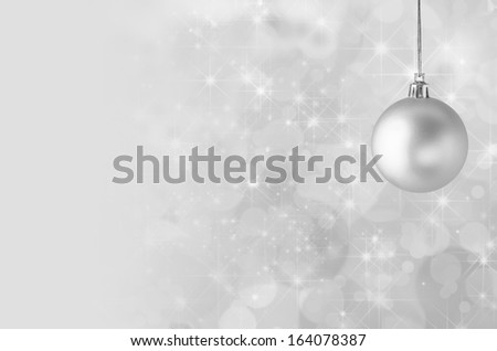 A silvery grey Christmas bauble, suspended on gold string against a star filled twinkly bokeh background, fading into solid colour to provide copy space on the left side.