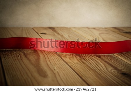 Close up of a red satin ribbon on an old wood plank table. Facing front to provide copy space for a message.  Parchment background.  Vintage style.