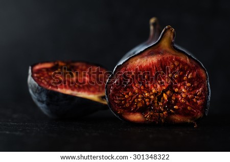Close up of well ripened figs, cut open to expose seeds and juicy innards.  Still life composition on black slate with black background.