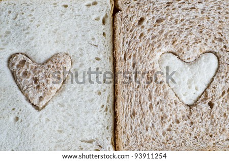 Close up of a white bread slice with a brown wholemeal heart, and a wholemeal bread slice with a white  heart.