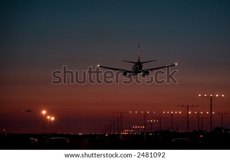 Twin engine passenger jet coming in for a landing during dusk, while another takes off in the distance